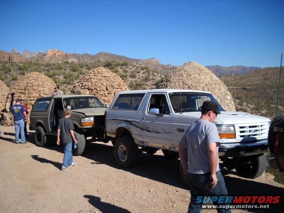 Two Ford Broncos parked on a dirt road with beehive-shaped structures in the background