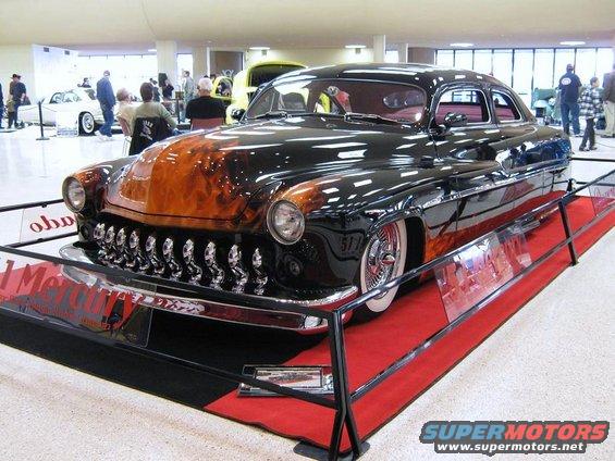 Black classic car with orange flame graphics on the hood and sides, displayed indoors