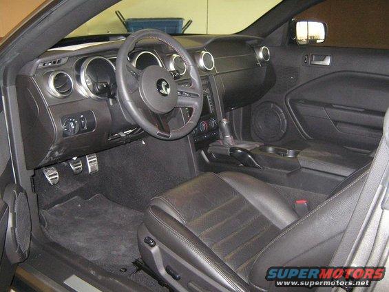 Interior shot of a car's dashboard, steering wheel, and seats. Shows a gear shifter and pedals