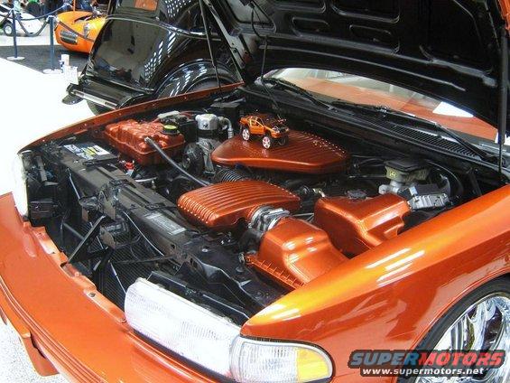 Orange engine bay with custom covers and a toy truck on top. Supermotors.net logo visible