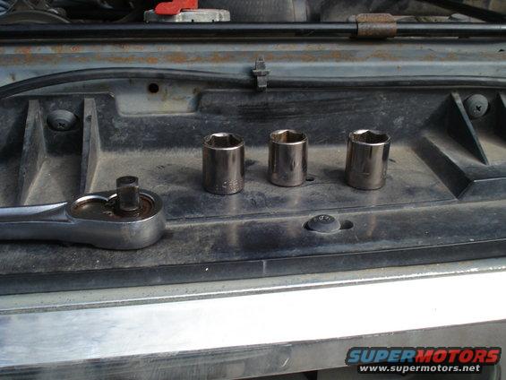 Socket wrench and three sockets on a black plastic surface, possibly in a vehicle's engine bay