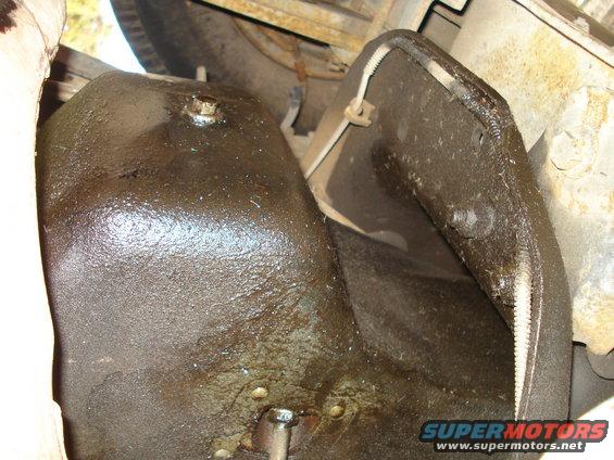 Underside of a vehicle showing a greasy oil pan and part of the exhaust system
