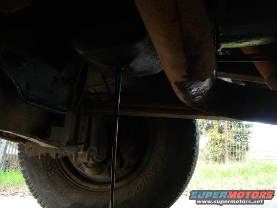 Underside of a vehicle with oil draining from the oil pan. A tire is visible