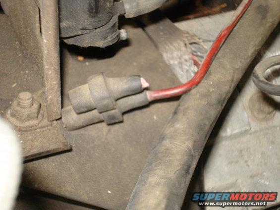 Close-up of a damaged red wire connected to a gray electrical connector in an engine bay