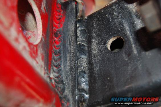 Close-up of welded metal frame with a hole. Red painted metal is visible on the left