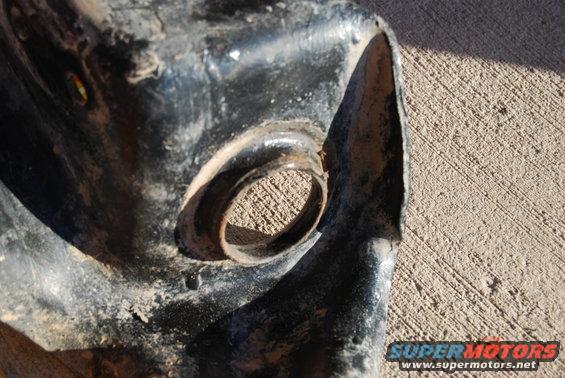 Close-up of a heavily rusted, black metal automotive part with a circular opening