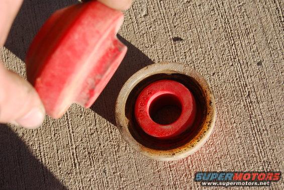 Hand holding a red rubber bushing over a metal housing with another red bushing inside. Text on the inner bushing reads '97824'
