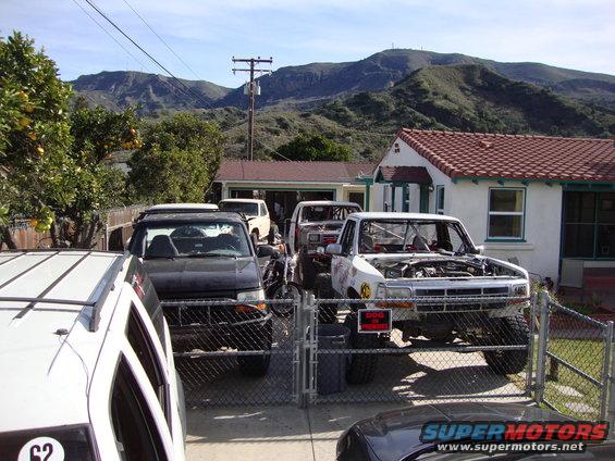 White off-road truck with hood open, parked behind a fence