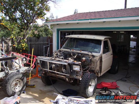 Ford F-Series truck, likely 1980-1986, with hood and fenders removed, parked in driveway next to another vehicle chassis