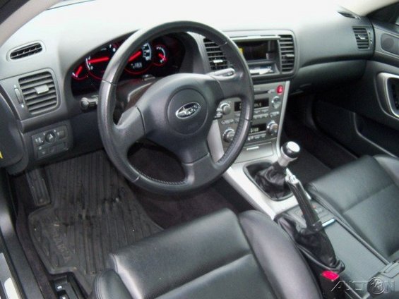 Interior view of a 2006 Subaru Legacy, showing the dashboard, steering wheel, center console with manual shifter, and leather seats