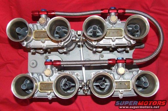 Dual Weber carburetors with red fittings and braided fuel lines on a red background