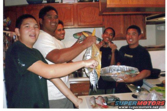 Group of men in a kitchen holding freshly caught fish