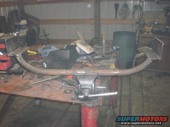 Custom trailer hitch receiver clamped in a vise on a workbench, with welding equipment nearby