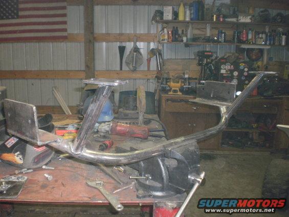 Metal frame part clamped in a vise on a workbench, with tools and an American flag in the background