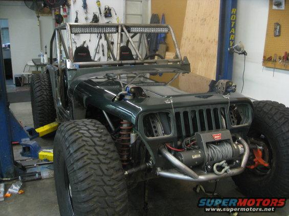 Green Jeep Wrangler with roll cage, large tires, and winch, in a garage