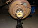 1971 International School Bus - Close-up of a heavily rusted wheel hub and brake assembly, resting on an automotive jack stand.