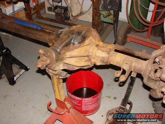 Rusty vehicle rear axle assembly on jack stands with a red bucket of fluid underneath