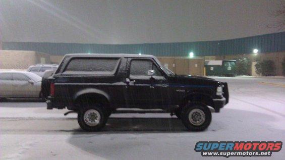 Black Ford Bronco parked in snow, side view. Another car is parked behind it