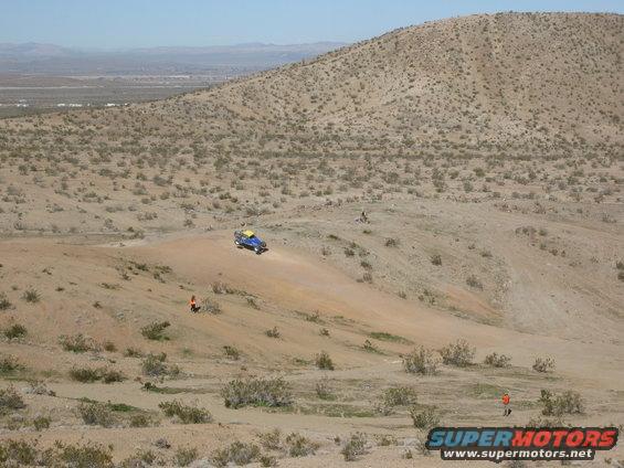 Blue off-road vehicle with yellow top driving on a dirt hill in a desert