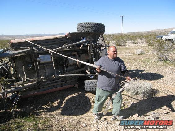 Overturned off-road vehicle with a man pulling a strap, another vehicle in background