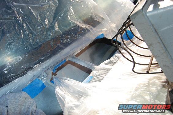 vehicle interior covered in plastic sheeting and blue tape, ready for paintwork