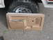 1981 Ford Bronco - A tan door panel is laid out on the ground in front of a vehicle's tire and fender.
