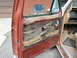 1981 Ford Bronco - Interior view of a red car door, showing worn upholstery and a speaker, with a glimpse of the dashboard and pedals.
