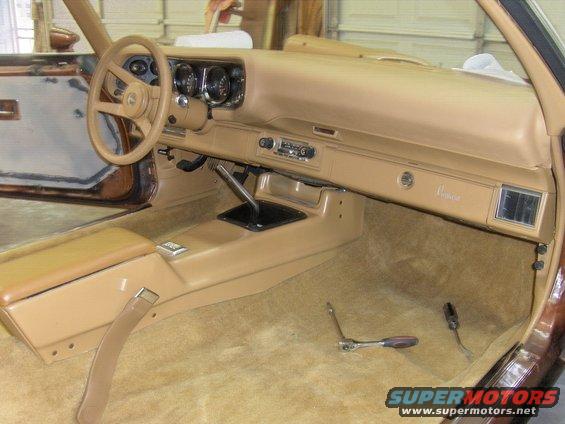 Interior of a 1982 Chevrolet Camaro, showing the dashboard, steering wheel, center console, and carpeting. Tools are on the floor