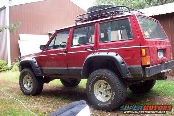 Red Jeep Cherokee XJ with roof rack and spare tire on top, parked outdoors