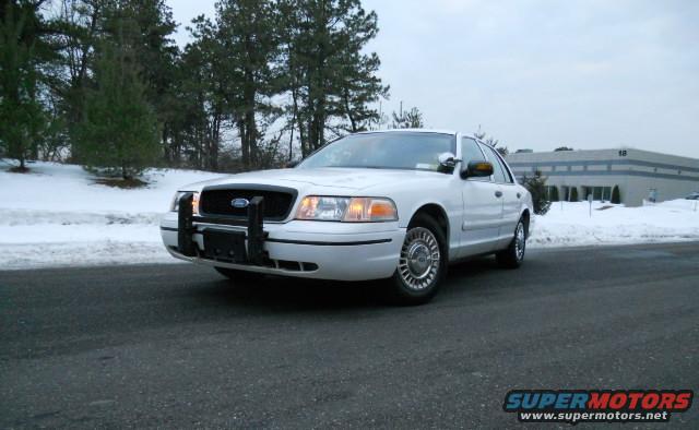 White Ford Crown Victoria with a push bar, parked on asphalt with snow in the background