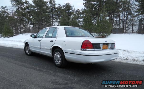 White sedan parked on a wet road with snow on the side, rear view