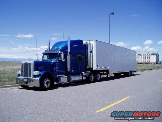 Blue semi-truck and trailer parked on the side of the road with a hotel in the background