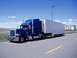 2009 Kenworth T800 - A blue semi-truck with a white trailer is parked on the side of a road under a blue sky with scattered clouds.