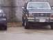 1985 Ford Bronco - A dark blue Ford Bronco is parked next to another vehicle, showing its front grille and headlights.