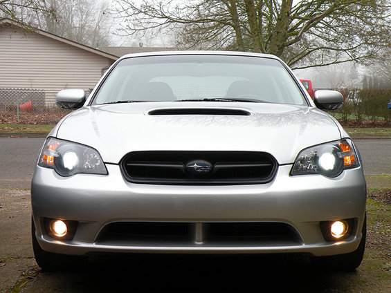 Front view of a silver Subaru sedan with headlights and fog lights on