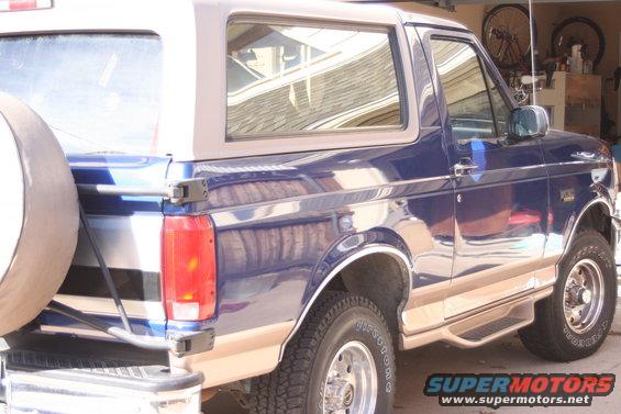 Blue 1996 Ford Bronco with tan trim and a spare tire on the rear, viewed from the rear three-quarter angle
