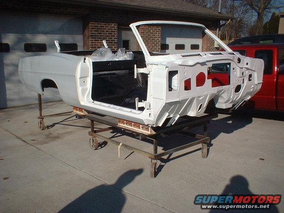 Car body on a stand, stripped down and primed white. Interior is blacked out