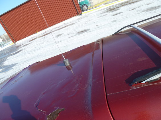 Red vehicle hood with antenna and visible rust damage