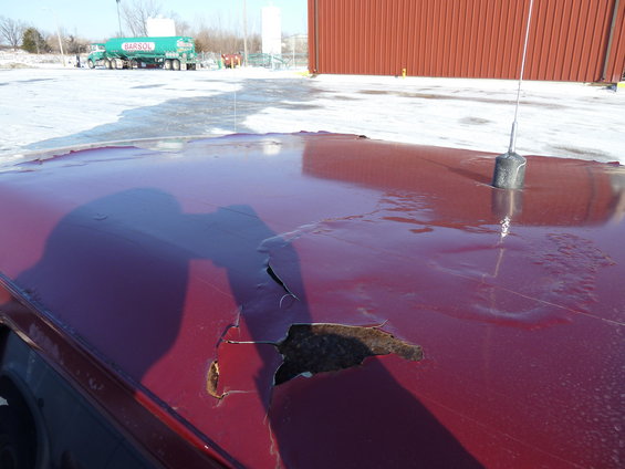 Close-up of a rusted-out section on a dark red car roof with an antenna