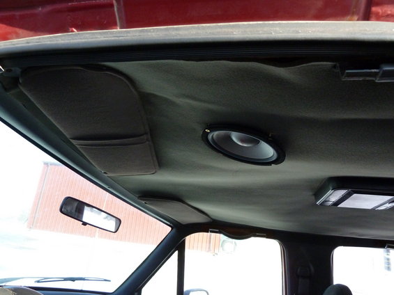 Interior shot of a vehicle's headliner with a speaker installed and a sun visor. A rearview mirror is visible