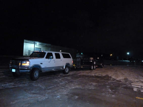 White extended cab pickup truck towing a trailer at night