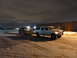 1993 Ford C-150 (Centurion Conversions) - A white Ford SUV tows a dark SUV on a trailer in a snowy lot at night.