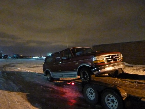 Maroon Ford Bronco SUV loaded onto a flatbed trailer at night