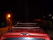 1993 Ford C-150 (Centurion Conversions) - The rear of a red SUV is visible at night, with a tall antenna extending from the roof.