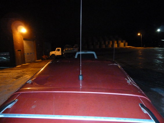 Red pickup truck roof with a long antenna and a white camper shell visible
