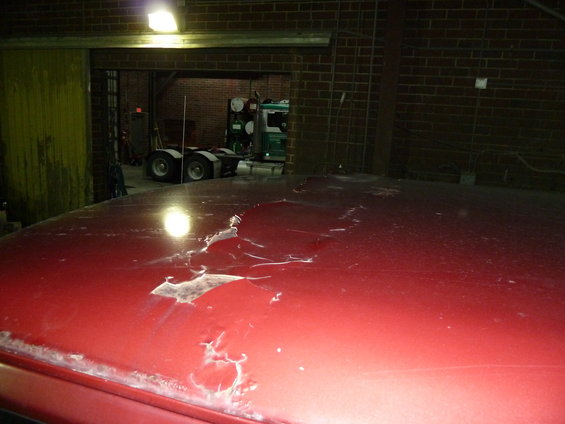 Red truck roof with peeling paint and visible damage. A semi-truck is parked in the background