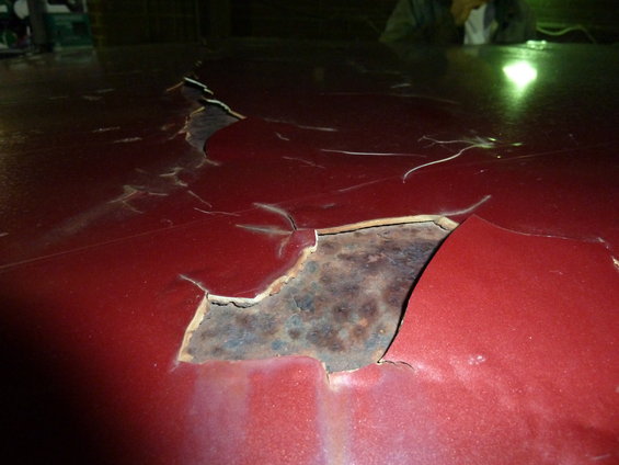 Red car roof with large areas of peeling paint revealing extensive rust underneath