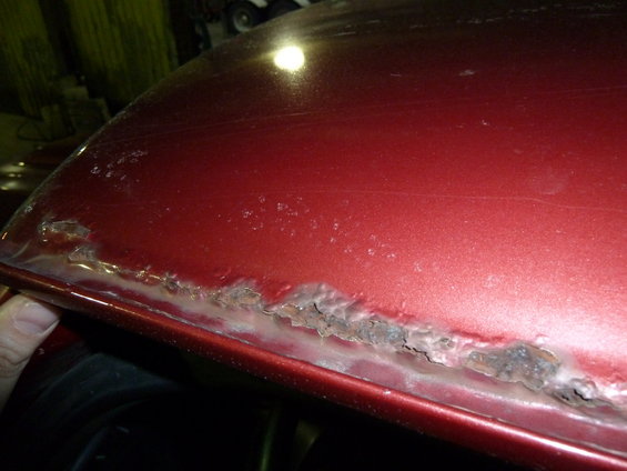 Close-up of severe rust damage along the edge of a red car body panel