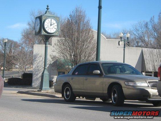Gold Mercury Grand Marquis parked by a clock tower