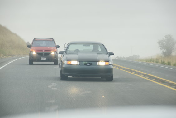 Dark sedan's front grille and headlights visible on a foggy highway